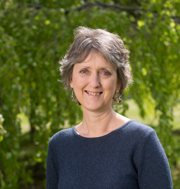 Zélie Cleaver, pain recovery specialist, smiling at the camera, on a sunny day outdoors with green foliage in the background.