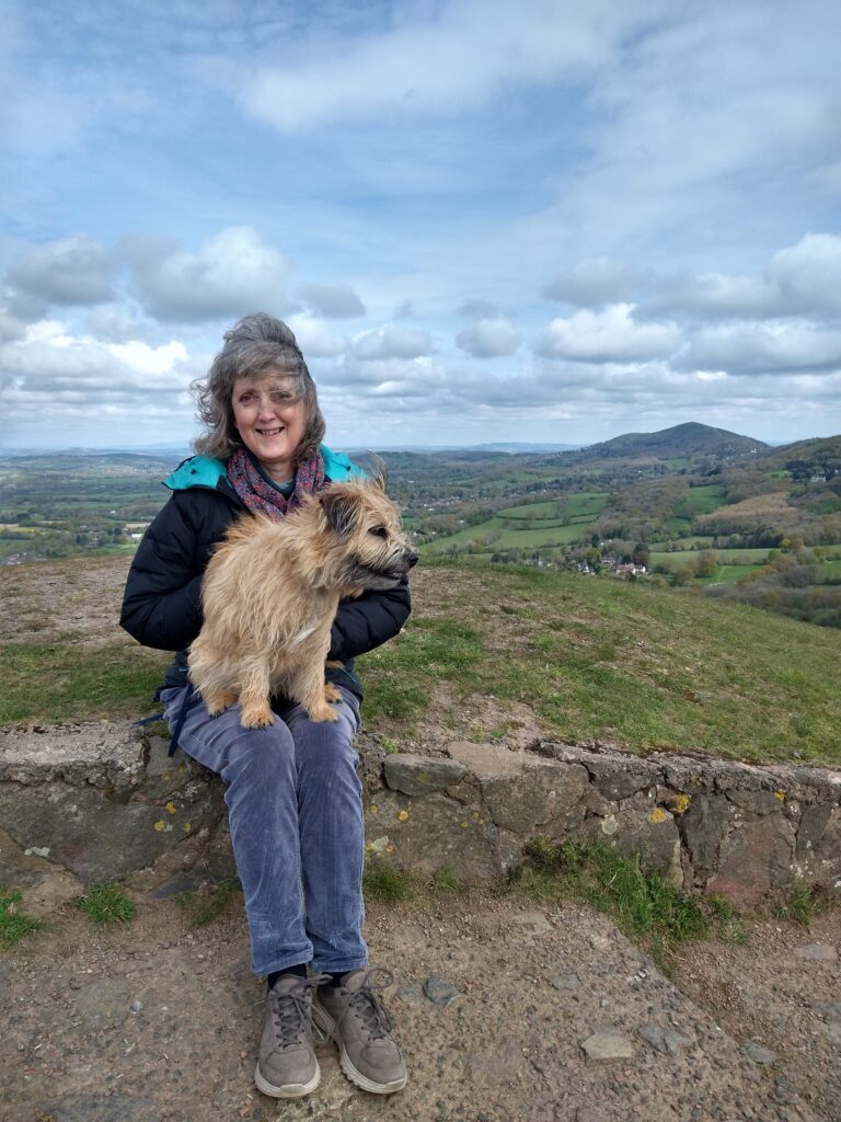 Zélie Cleaver, chronic pain recovery coach, sat at the top of a hill in the sunshine smiling at the camera.